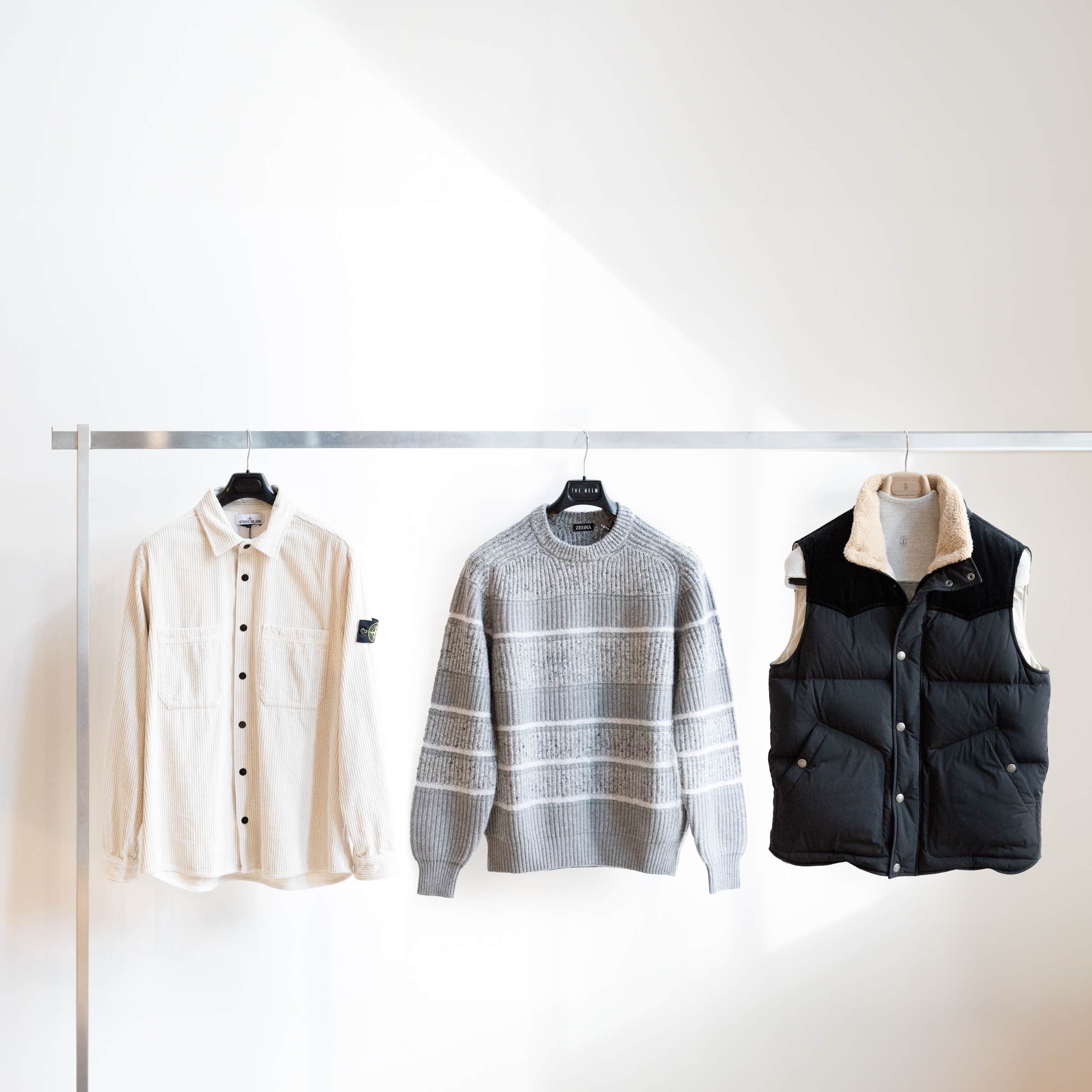 A Stone Island overshirt, ZEGNA sweater and Brunello Cucinelli vest hanging on a clothes rack